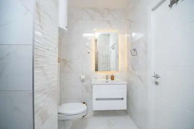 a white bathroom with a toilet and a sink at Hemingway LUX in Arandjelovac