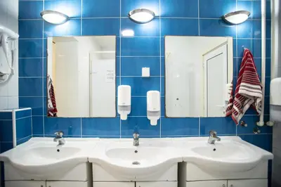 two sinks in a blue tiled bathroom with two mirrors at All in Hostel in Belgrade