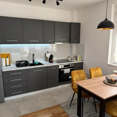 a kitchen with black cabinets and a wooden table at JR Lux apartman in Stara Pazova