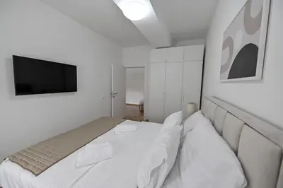 a white bedroom with a bed and a television at Porto lux in Arandjelovac