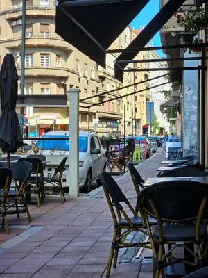 an outdoor cafe with chairs and tables and an umbrella at HostGost Selected Suites – Parliament in Belgrade