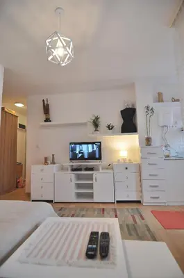 a living room with a television and white furniture at Charming studio near downtown in Belgrade