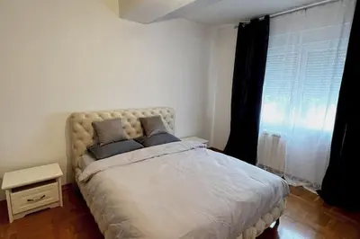 a bedroom with a large white bed with a window at Biser apartman in Belgrade