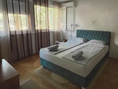 a bed with a blue headboard in a room with windows at Apartman Sasha 2 in Belgrade