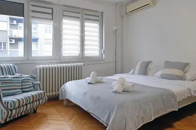 a bedroom with two beds and a chair and a window at Vintage Dream Apartment in Belgrade