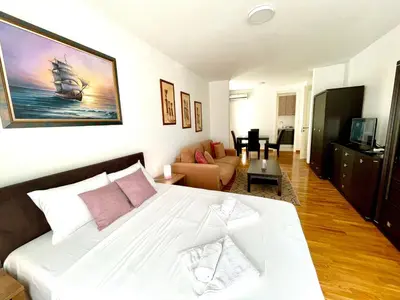 a bedroom with a large white bed and a living room at Modesti - stan na dan Novi Beograd sa parkingom 5 evra po danu in Belgrade