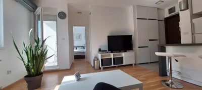 a white living room with a tv and a table at Miyaki Apartment in Belgrade