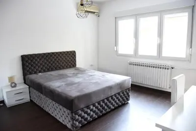 a large bed in a white room with two windows at Lux Flat Center in Belgrade