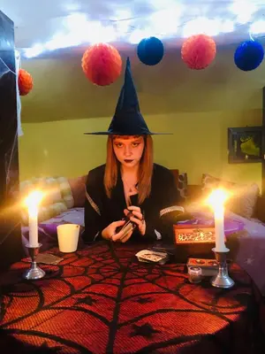 a woman wearing a witches hat sitting at a table with candles at Hostel El Diablo in Belgrade