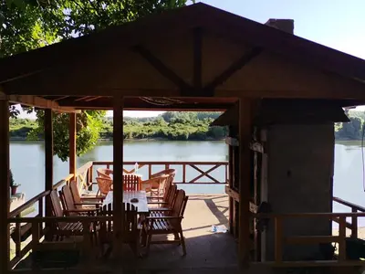 a table and chairs under a pavilion next to a lake at Vikendica Tisa Dukatar in Titel