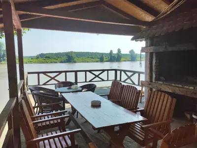 a wooden table and chairs on a porch next to a lake at Vikendica Tisa Dukatar in Titel