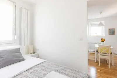 a white bedroom with a bed and a desk at Apartment Artistique in Belgrade