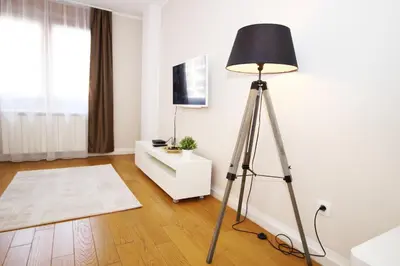 a tripod floor lamp in a white room with a tv at Apartment A Block Nota Delta City New Belgrade in Novi Beograd