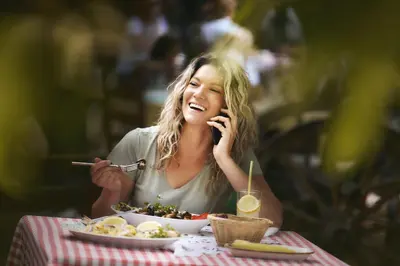 a woman sitting at a table talking on a cell phone at Wood Mood Apartman Tiganjica in Staji°evo