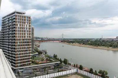 a tall building next to a river with a bridge at SINFONIA LUX in Belgrade