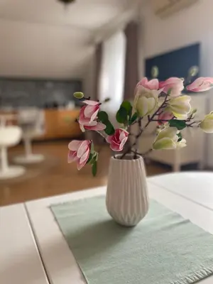 a white vase with pink flowers sitting on a table at Apartman Magnolia in Zemun
