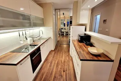 a kitchen with white cabinets and a wooden floor at Apartman Meri in Tošin Bunar