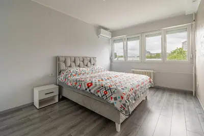 a white bedroom with a bed and a window at Apartman Ivana in Novi Beograd