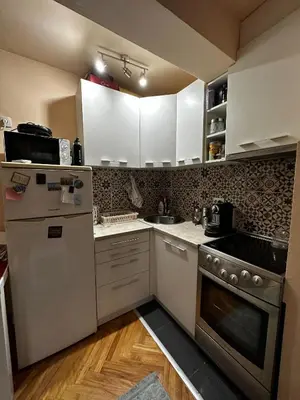 a small kitchen with white cabinets and a refrigerator at Cozy loft in Belgrade