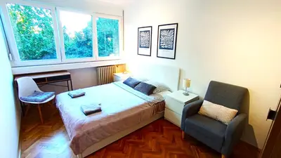 a bedroom with a bed and a chair and two windows at ParkWest Arena Belgrade Lux Apartment in Belgrade