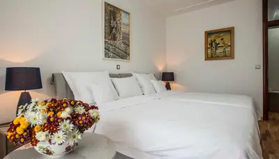 a white bed with a vase of flowers on a table at Hotel Radmilovac in Belgrade