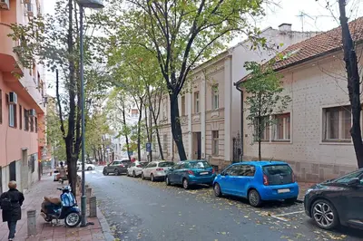 a man riding a scooter on a street with parked cars at Relax Home Downtown Apartment in Belgrade