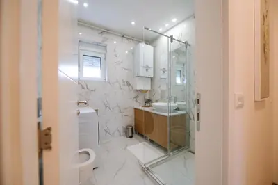 a bathroom with a glass shower and a sink at Nika apartman in Surčin