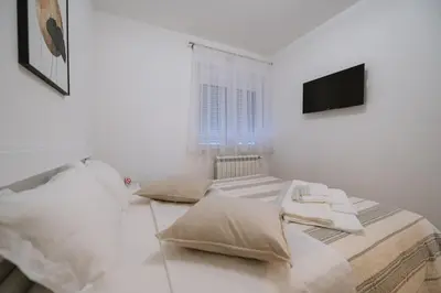 a white bedroom with two beds and a television at Nika apartman in Surčin