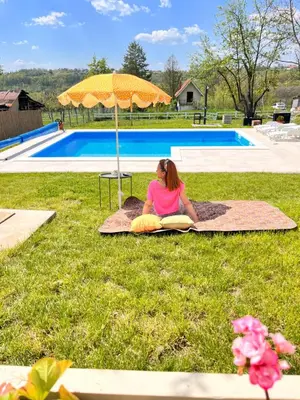 a woman sitting on the grass under an umbrella at Vila blizu Beograda - My Family Cottage in Ba°evac