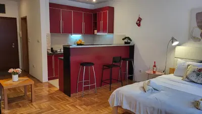 a bedroom with a bed and a kitchen with red cabinets at Bulevar Plus in Belgrade