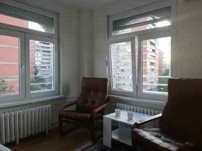 a living room with two chairs and a table and windows at Atelje 11 in Belgrade