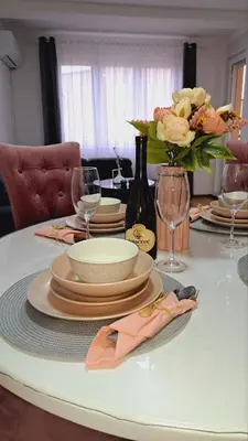 a table with plates and glasses and a vase of flowers at Maja 2 in Ruma