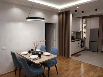 a dining room table with blue chairs and a kitchen at Lider Lux Apartman in Arandjelovac