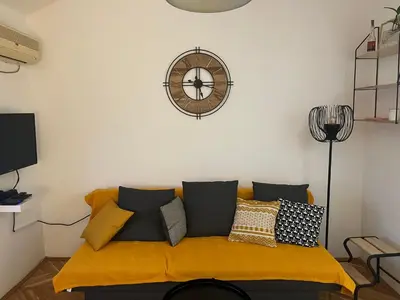 a living room with a yellow couch with a clock on the wall at Apartman Stevan in Pančevo