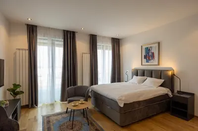 a bedroom with a bed and a chair and windows at Belgrade Center Apartment Lux 1 in Belgrade
