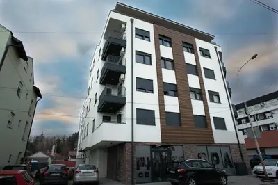 a tall white and brown building with cars parked in a parking lot at Apartman Ub in Ub