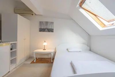 a small white bedroom with a bed and a table at Downtown nest in Belgrade