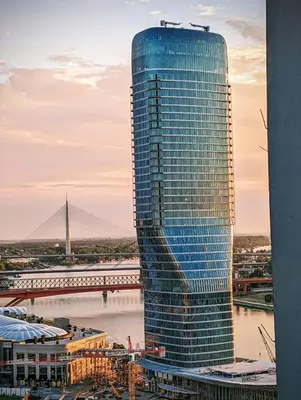a tall glass building next to a river at Belgrade Waterfront Victory Gardens in Sajmište