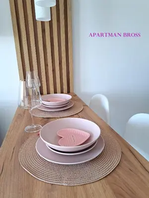 a wooden table with two plates and glasses on it at Apartman Bross in Ruma