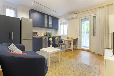 a living room with a blue chair and a kitchen at The 7 Apartment - Modern Flat with Terrace near Parliament, Belgrade Center in Belgrade