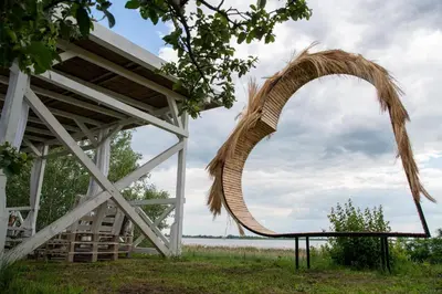 a large wicker arch in a field next to a building at Carska oaza in Lukino Selo