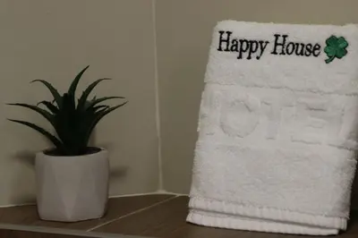 a white towel with a happy house sign next to a plant at AIRPORT APARTMANI HAPPY HOUSE free parking & early check-in in Surčin