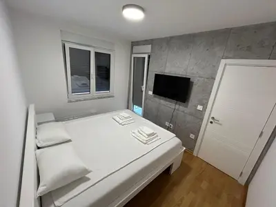 a small bedroom with a white bed and a tv at Apartman ARISTEA in Arandjelovac