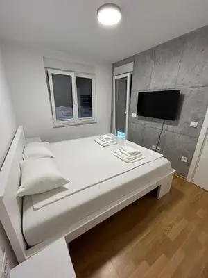 a large white bed in a room with a flat screen tv at Apartman ARISTEA in Arandjelovac