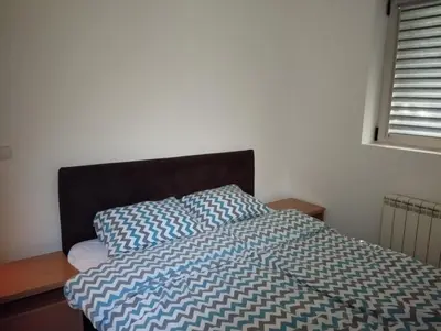 a bed with a blue and white comforter and a window at Apartman Nera in Stara Pazova