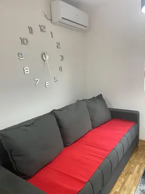a black couch in a room with a clock on the wall at Apartman Fame near Airport in Surčin