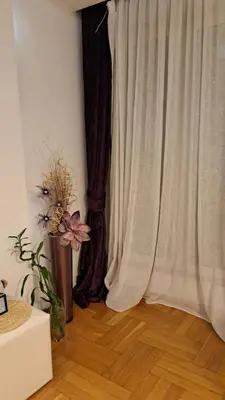 a room with a curtain and a vase with flowers at Lux Apartman 7 in Voždovac