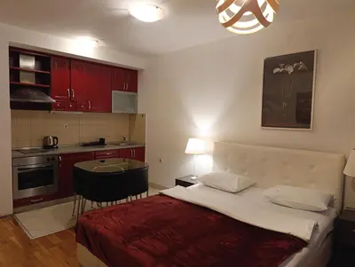 a bedroom with a bed and a kitchen with red cabinets at Kala in Belgrade