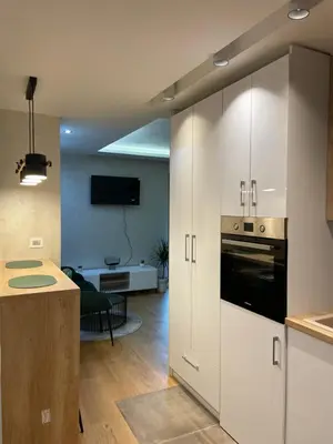 a kitchen with white cabinets and a living room at Apartments Jedro in Belgrade