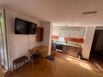 a kitchen with a table and a television on the wall at Apartment GreenTerrace next to TC BIG FASHION Mall in Karaburma